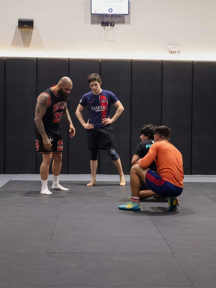 A coach demonstrating a stance to three students on Mat 1