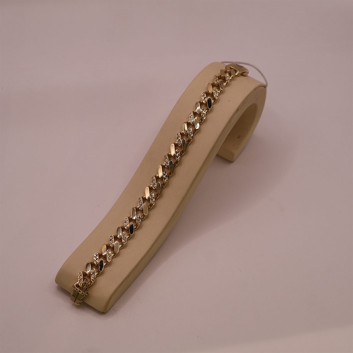 Flat gold link bracelet laid along a display stand