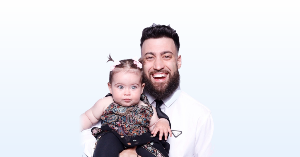 DRHOBS (Guy Hobaika) holding his daughter Amara, on a light blue gradient background